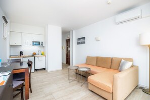 A compact living space with a kitchenette, a sofa, a dining table, and a lamp. - Apartment 'Sea View Room 106' with Shared Pool, Wi-Fi and Air Conditioning (Portocolom)