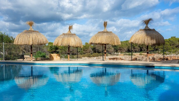 Une piscine dotée de quatre parasols en chaume et d’une zone délimitée par une clôture.
