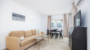 A living room with a sofa, two small tables, a TV, and a dining area with chairs and a table. - Apartment 'Pool View Room 101' with Shared Pool, Wi-Fi and Air Conditioning (Portocolom)