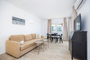 Una sala de estar con un sofá, dos mesitas, un televisor y un comedor con sillas y una mesa.