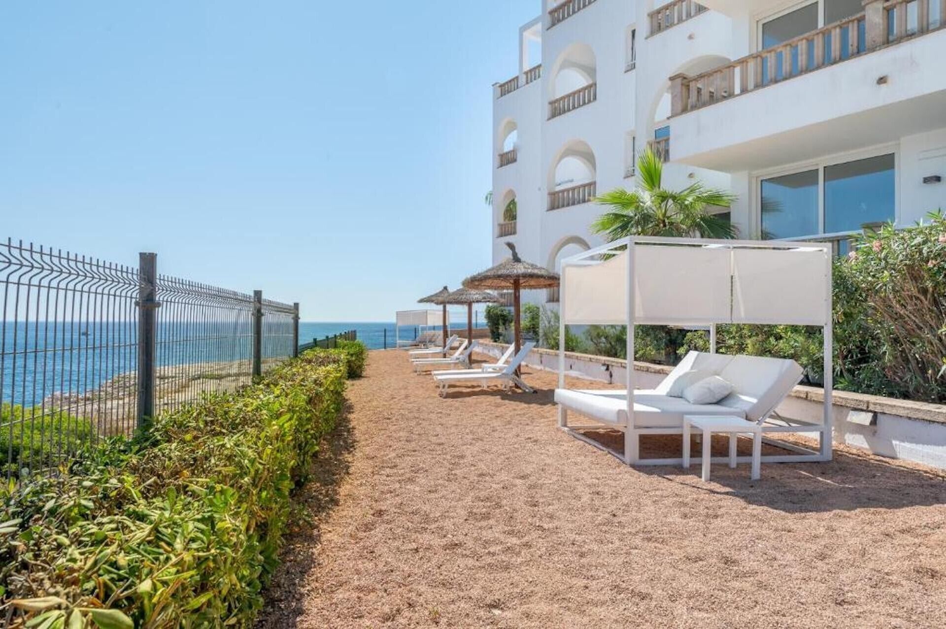 Un hôtel situé en bord de mer, doté de chaises longues, d’une promenade piétonne délimitée et offrant une vue sur la mer.