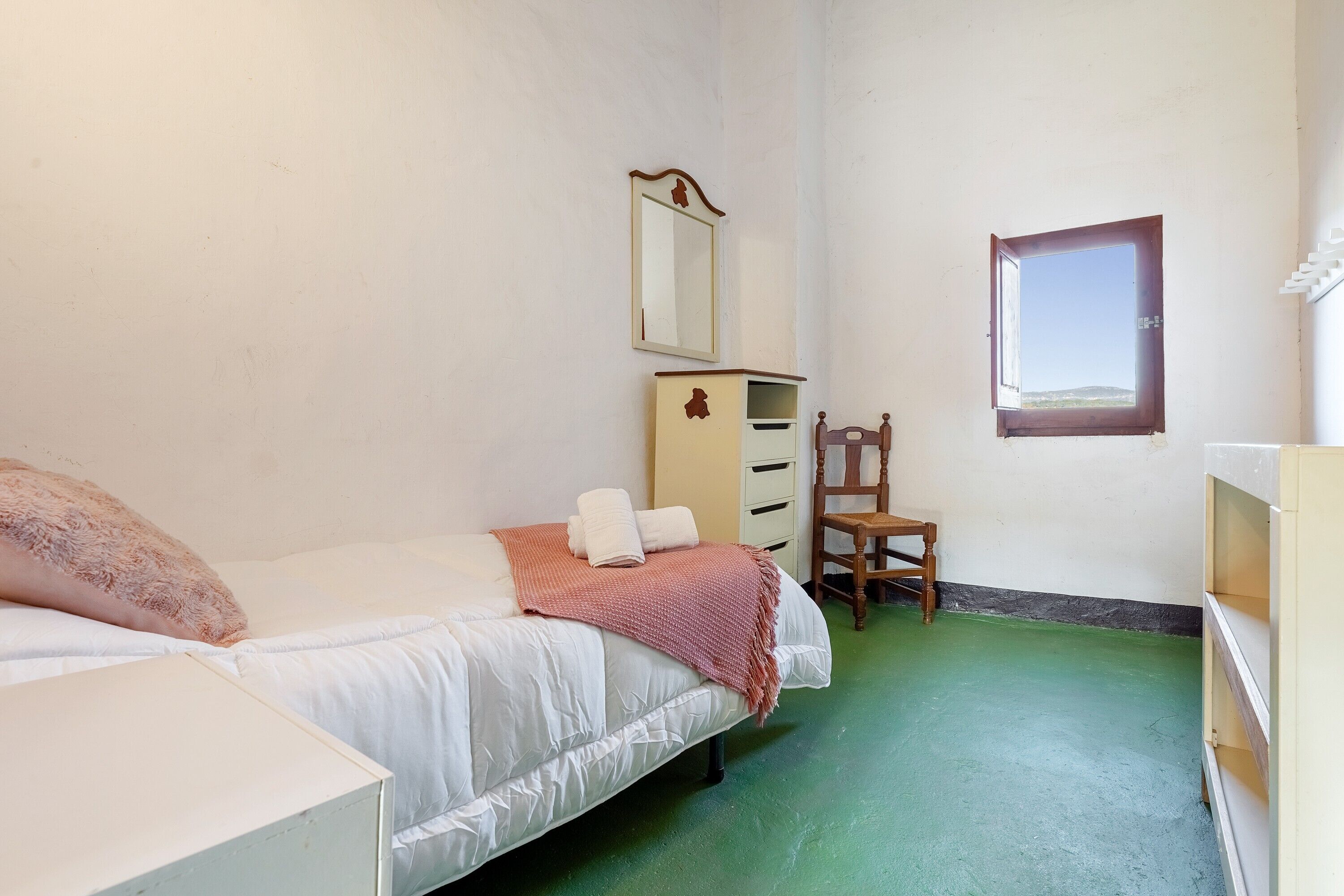 Une chambre à coucher avec un lit, une commode, une chaise, un miroir et une fen être.