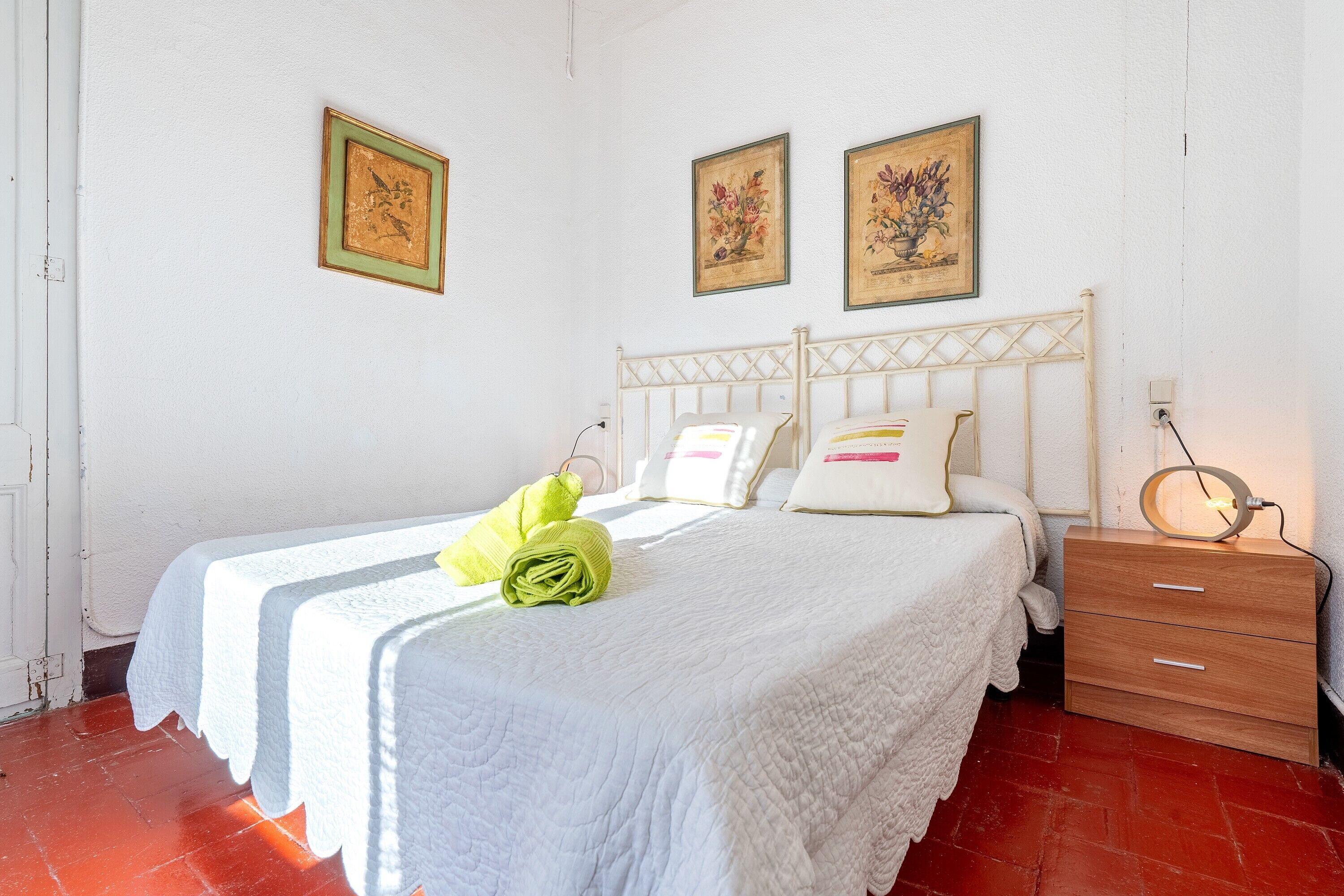 A bedroom with a bed, a wooden nightstand, a white wall, and two framed pictures.
