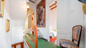 Een gang met een groen tapijt, een houten leuning, een stoel met een gestreept rugleuning en een schilderij aan de muur.
