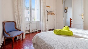 Een kamer met een bed, een stoel, een raam met gordijnen en een deur.