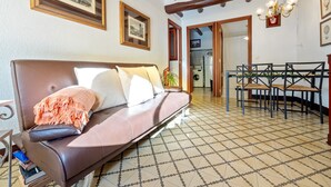 Een woonkamer met een bank, een eethoek met stoelen en een betegelde vloer.