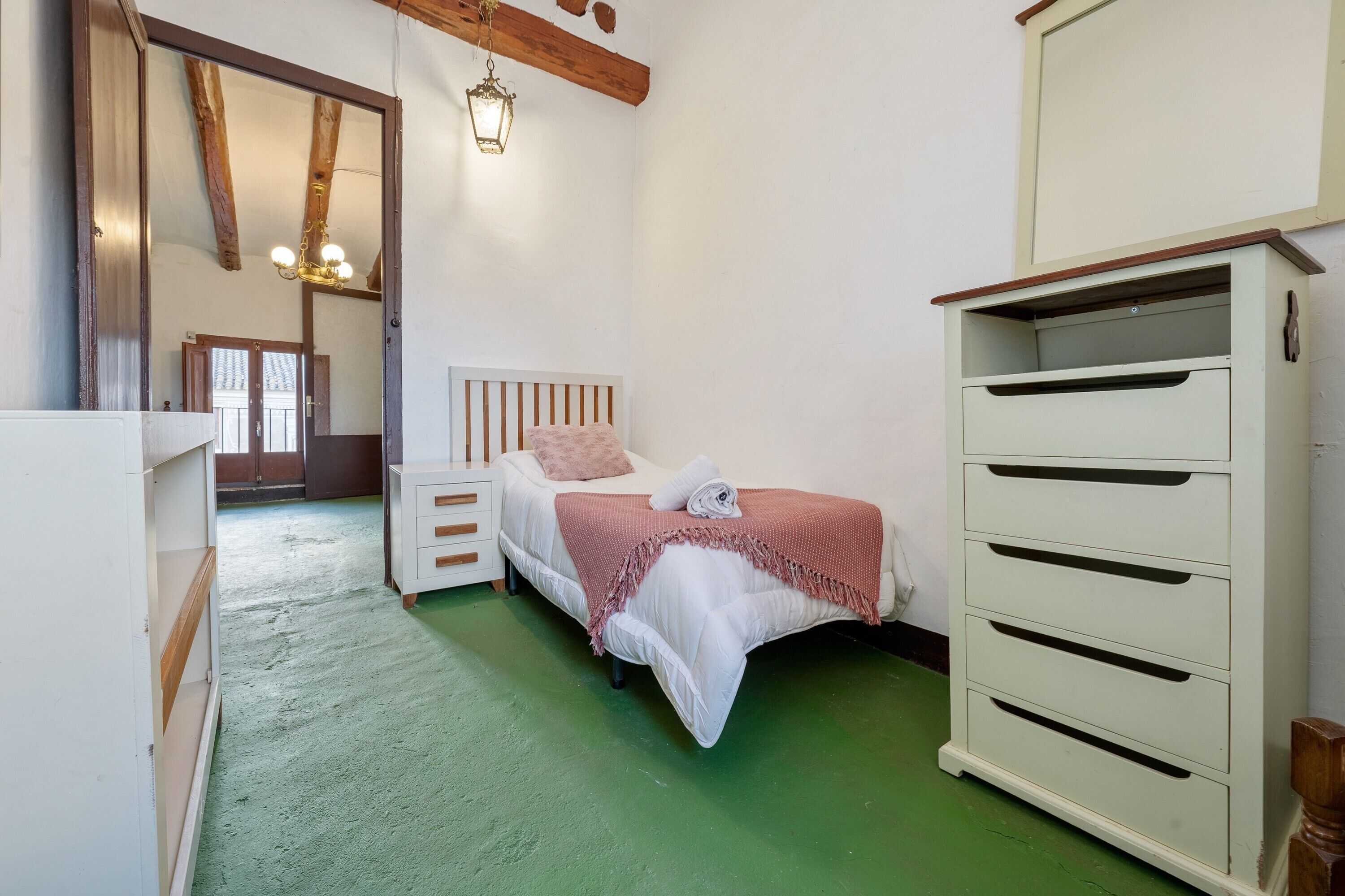 Une chambre à coucher avec un lit, une commode, un miroir et une poutre en bois au plafond.