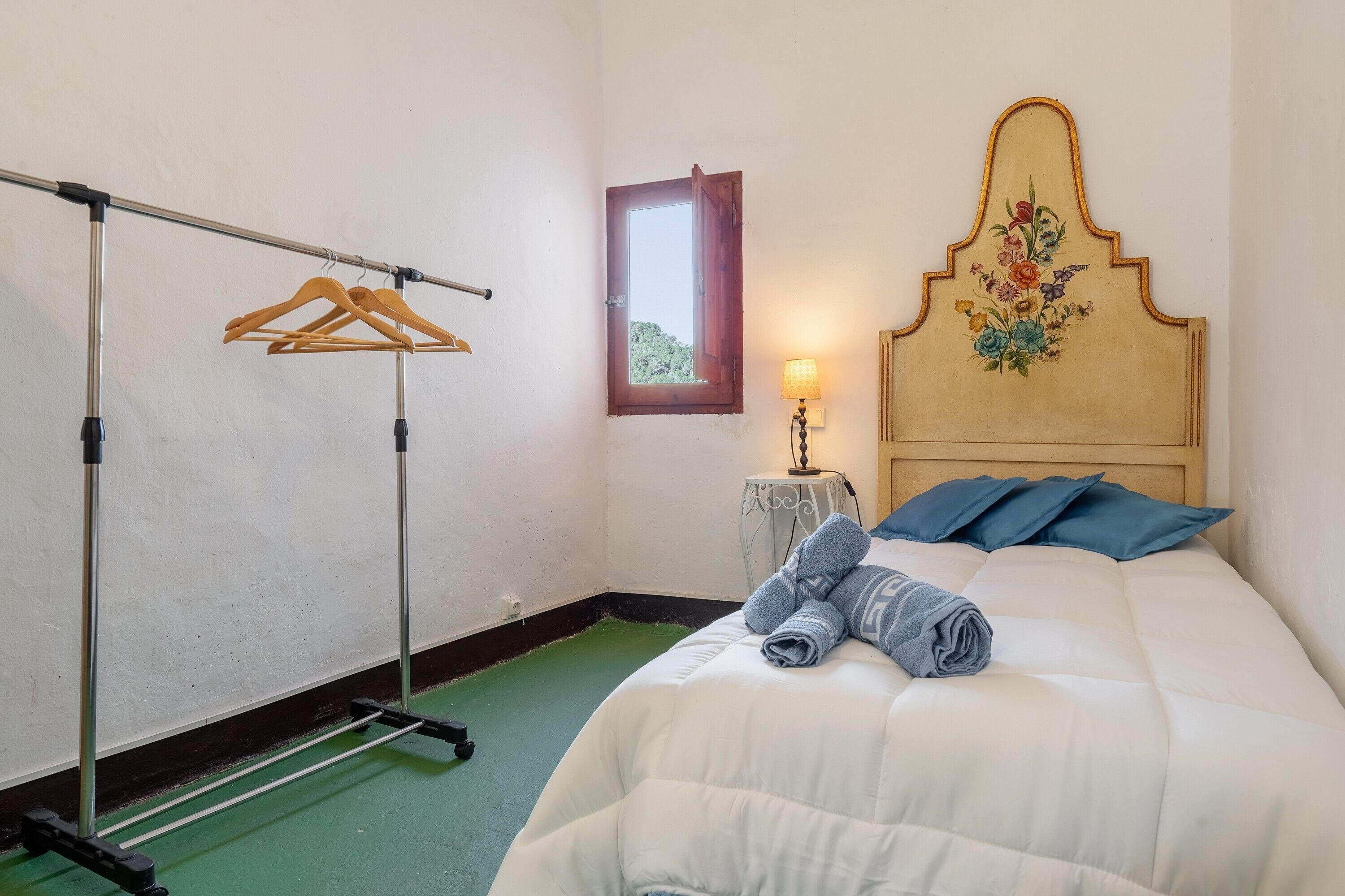 A hotel room with a bed, a hanging clothes rack, a small table with a lamp, and a window with a view.