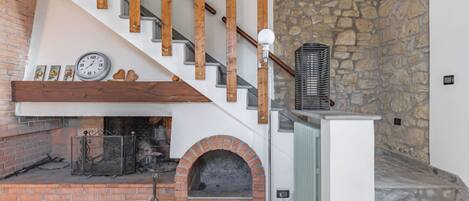 A staircase with wooden handrails, a brick fireplace with a clock, and a stone wall.
