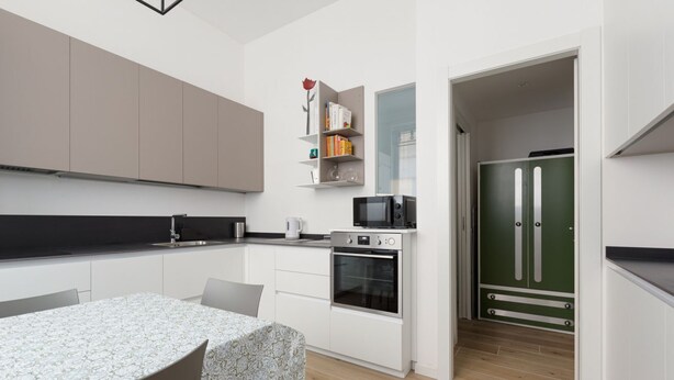 A modern kitchen with white cabinets, a dining table, and a green door.
