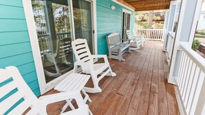 A covered porch with white plastic chairs and a table, wooden deck, and a turquoise building facade. - Soundside, ELEV, Priv Pool, Hot Tub, Community Amenities- MS853, Resting Beach Place (Corolla)