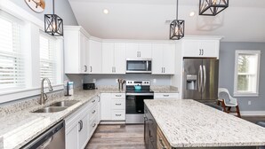 A modern kitchen with white cabinets, stainless steel appliances, granite countertops, and pendant lighting. - Soundside, ELEV, Priv Pool, Hot Tub, Community Amenities- MS853, Resting Beach Place (Corolla)