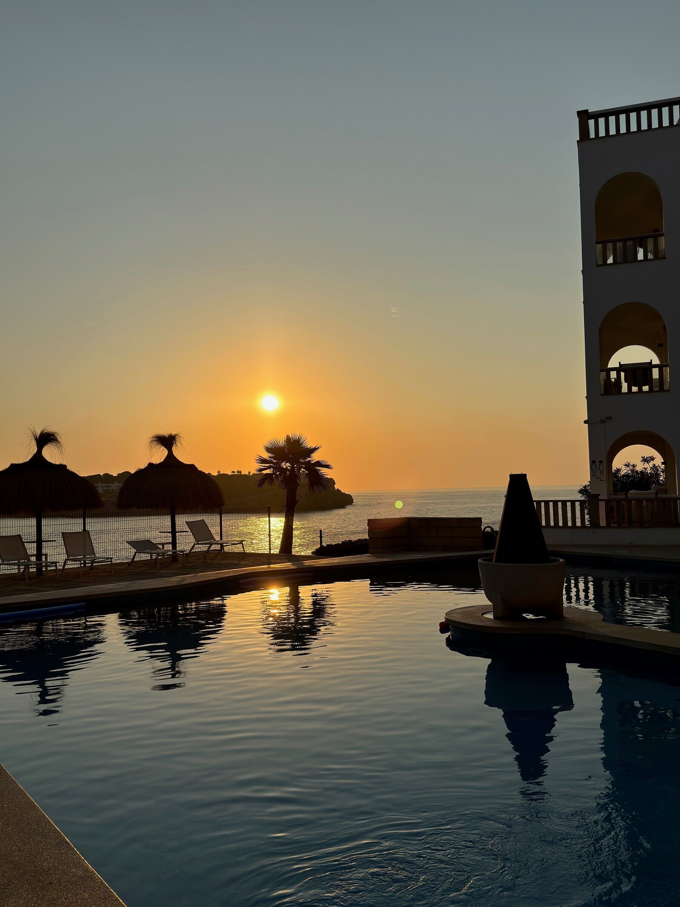 A pool with a sunset view, lounge chairs, and a building with arches.