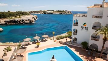 Un hotel con piscina, sillas de descanso, sombrillas y vistas al mar.
