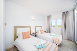 Habitación de hotel con dos camas, una ventana con cortinas, una mesita de noche con lámpara y una toalla en el suelo.