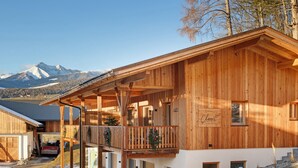 A wooden chalet with a balcony, a garage, and a mountain view in the background.