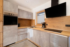 A modern kitchen with a built-in oven, a coffee maker, and a flat-screen TV mounted on the wall.