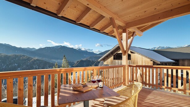 A wooden deck with a table and chairs, a bottle of wine, and a basket of bread.
