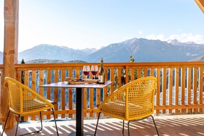 Un balcon avec deux fauteuils en osier jaune, une table et une bouteille de vin.