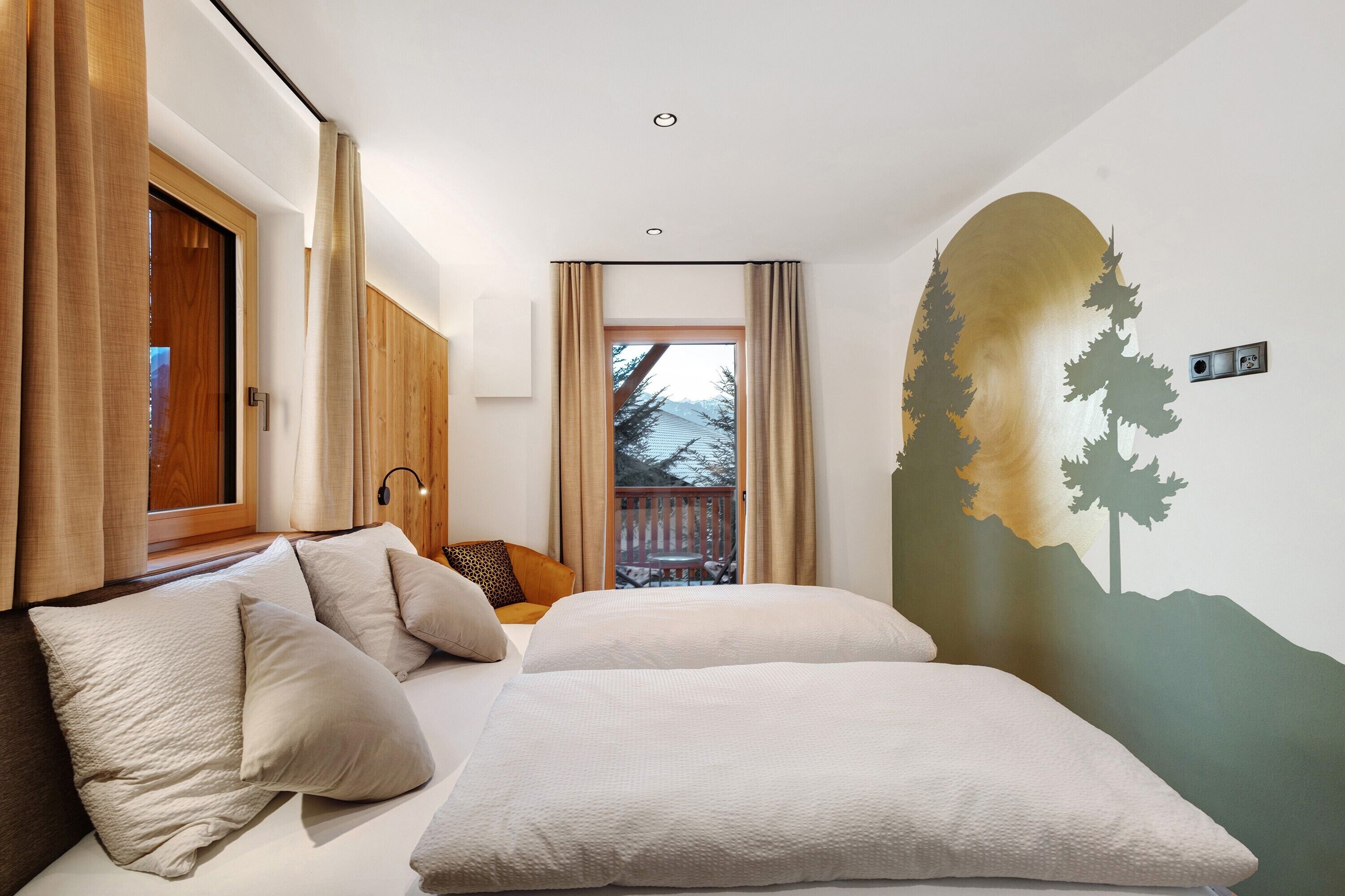 A bedroom with a bed, pillows, a wooden door, a window with curtains, and a wall mural.