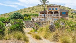 Ein zweistöckiges Haus mit Balkon, umgeben von trockenem Gras und einer Palme.