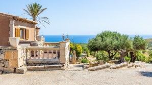 Ein Küstengebäude mit einer Steintreppe, einer Palme und Blick auf das Meer.