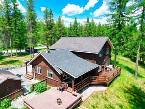 A cabin with a deck, a covered porch, and a large window overlooking a forest.