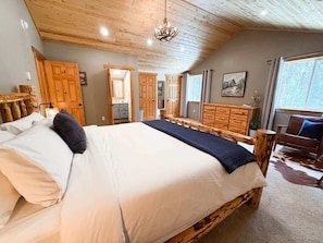 A bedroom with a large bed, wooden furniture, a chandelier, and a view of the outdoors.