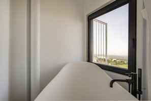 A modern bathroom with a bathtub, a window with a view of buildings, and a black faucet.