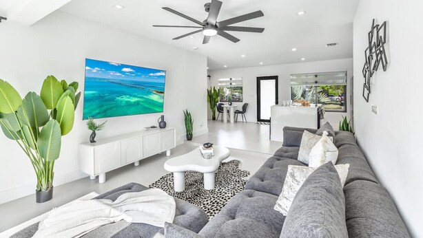 Ein modernes Wohnzimmer mit einem großen Flachbildfernseher, einem Deckenventilator und einem grauen Sofa.