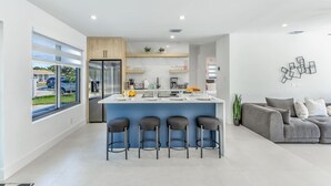 Eine moderne Küche mit einer zentralen Kochinsel, Barhocker und einem grauen Sofa in einem hellen Wohnbereich.