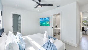 Ein modernes Schlafzimmer mit Bett, Deckenventilator, Fernseher und einem durchgegangenen Tür sichtbaren Badezimmer.