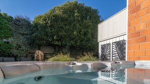 A hot tub with a clear view of the surrounding area, including a brick wall and a large tree. - Close to Beach | Spacious | Outdoor Living - KK00379 (Kaikoura)