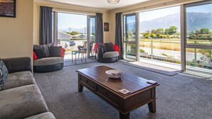 A spacious living room with a large window, a wooden coffee table, and two sofas. - Close to Beach | Spacious | Outdoor Living - KK00379 (Kaikoura)
