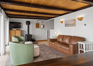 A cozy living room with a fireplace, a leather sofa, a green armchair, and a television. - Sandpiper Cottage Beautiful Private Lake Michigan Frontage (Mears)
