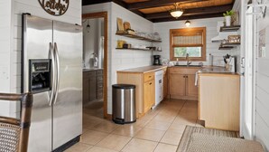 A kitchen with a stainless steel refrigerator, wooden cabinets, a sink, and a trash can.