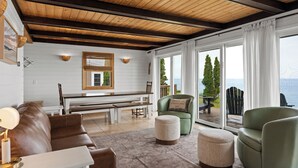 A cozy living room with a wooden ceiling, a bench, a green armchair, and a view of the sea.