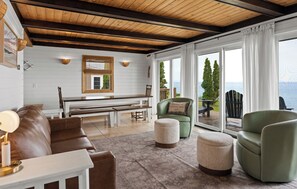 Uma sala de estar acolhedora com teto de madeira, um banco, uma poltrona verde e vista para o mar.