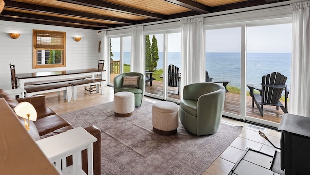 A spacious living room with a piano, seating area, and large windows overlooking the sea.
