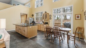 Een ruime keuken met een centraal eiland, houten kastjes en een eethoek met stoelen en een tafel.