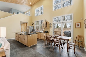 A spacious kitchen with a central island, wooden cabinets, and a dining area with chairs and a table.