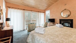 Een slaapkamer met een bed, een televisie, een open haard en een balkon met gordijnen.