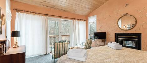 Une chambre à coucher comprenant un lit, une télévision, une cheminée et un balcon avec des rideaux.