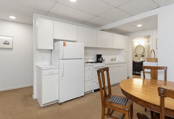 A compact kitchen with white cabinetry, a refrigerator, a coffee maker, and a dining table with chairs.