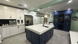 A modern kitchen with white and dark blue cabinetry, stainless steel appliances, and a central island with a sink. - Island Chic Vacation Manor in the tranquil community of Coral Harbour, Bahamas (Nassau)