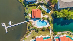 Eine Luftaufnahme eines Resorts mit Schwimmbad, einer Anlegestelle mit einem Boot und umgebender Bepflanzung.