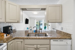 A kitchen with white cabinets, a granite countertop, a double sink, and a dishwasher.