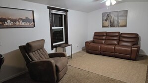 Un salon avec un canapé en cuir marron, un fauteuil inclinable, une petite table et un ventilateur de plafond.