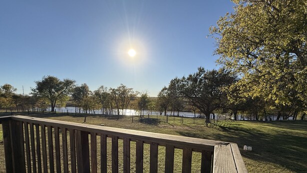 Une terrasse en bois donnant sur une zone verdoyante, avec des arbres et une étendue d’eau.