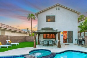 A two-story house with a swimming pool, a patio with chairs, and a covered outdoor seating area. - Vegas Getaway 3BD Home- Pool & Garage Parking (Henderson)